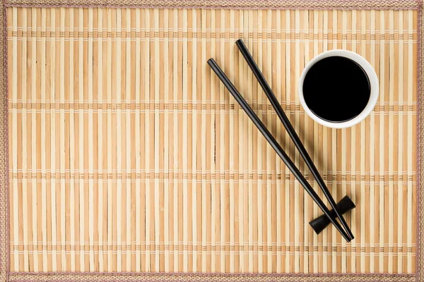 Chopsticks e tigela com molho de soja na esteira de bambu — Fotografia de Stock