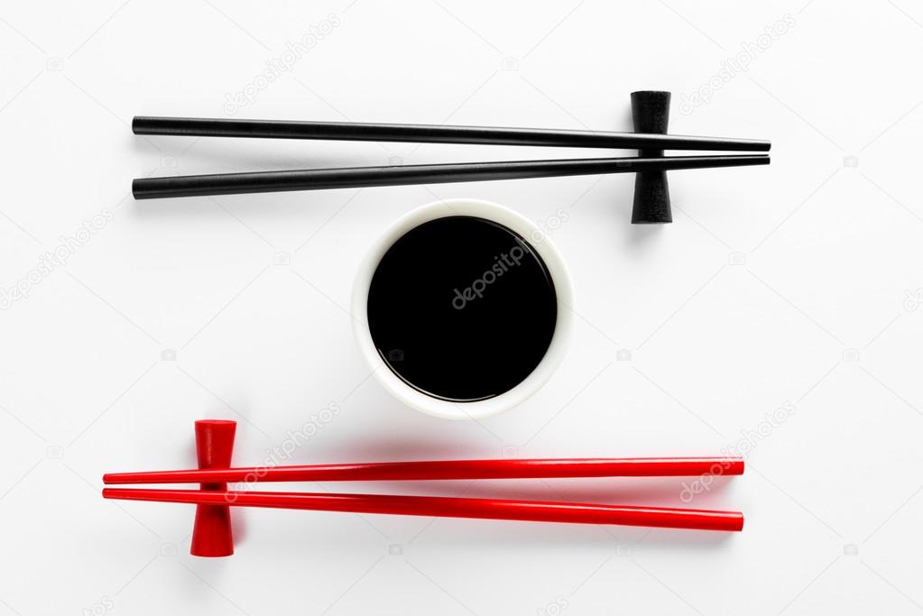Chopsticks and bowl with soy sauce on white background