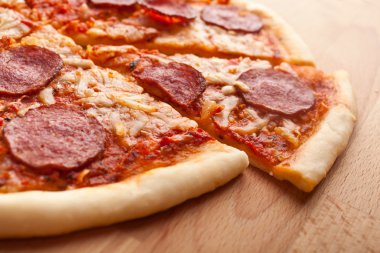 Bütün salamlı pizza tahta masanın üzerine dilimlenmiş
