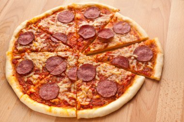 Bütün salamlı pizza tahta masanın üzerine dilimlenmiş