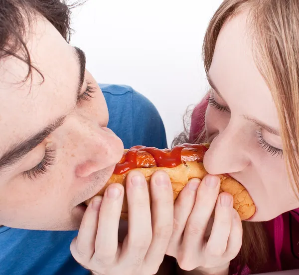 Jovem casal comer o mesmo cachorro quente — Fotografia de Stock