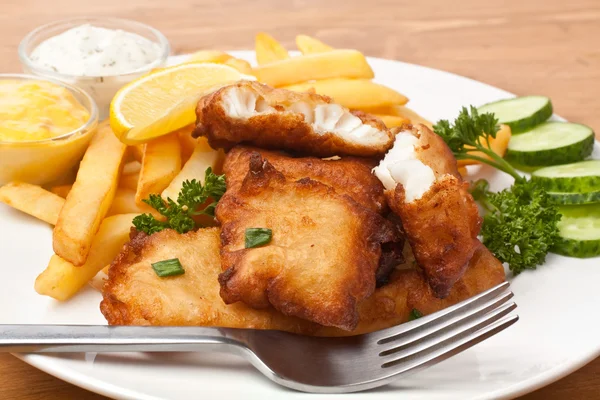 Pesce e patatine fritte su un piatto su un tavolo di legno — Foto Stock