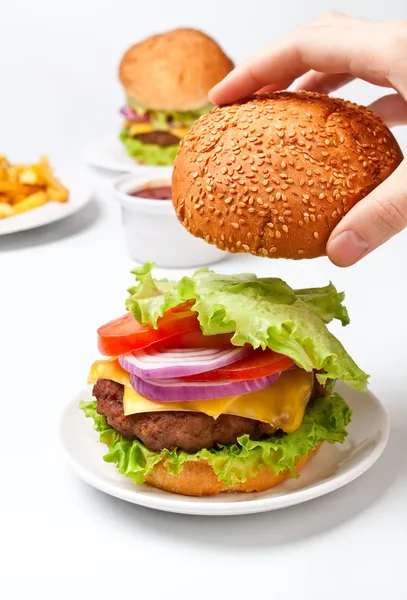 Hand legt das obere Brötchen auf einen großen leckeren Cheeseburger — Stockfoto