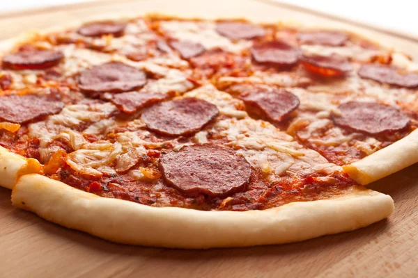 Sliced whole salami pizza on a wooden table — Stock Photo, Image