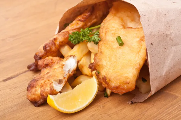 Pesce e patatine avvolti in carta su un tavolo di legno — Foto Stock