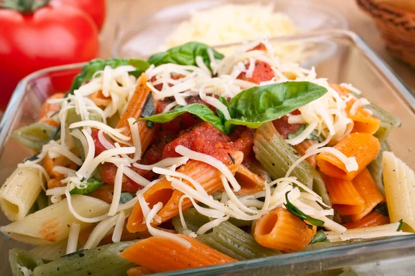 Servering av farget pasta med tomatsaus og basilikum – stockfoto