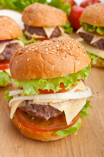 Group of cheeseburgers, with ingredients on wooden table — Stock Photo, Image