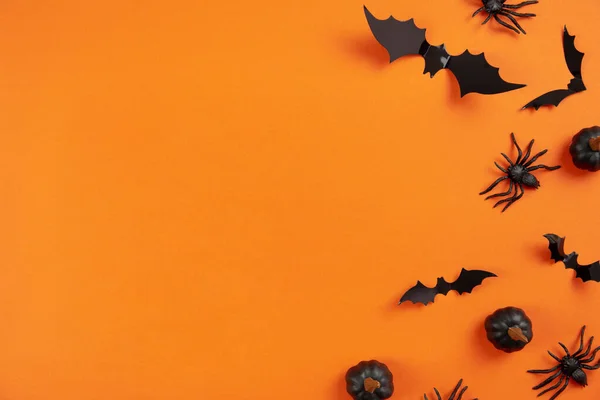 Happy halloween flat lay mockup with black pumpkins, spiders and bats on orange background. Holiday concept composition. Top view. Copy space.