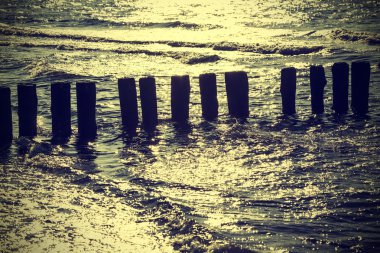 Wood pilings in water against sun, vintage retro instagram effec clipart