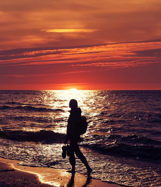 Žena kráčí po pláži při západu slunce. — Stock fotografie