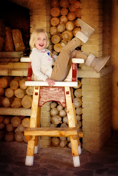 Little cute girl sitting on a chair near the fireplace — Stock Photo, Image