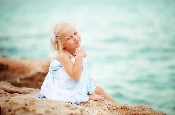 Little girl sitting on a rock by the sea — Stock Photo, Image