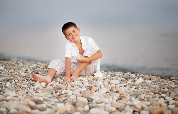 Jongen zit op stenen seacoastby in de buurt van de zee — Stockfoto