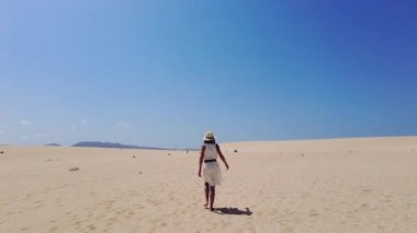 Genç bir turist, Fuerteventura, Kanarya Adaları 'ndaki Corralejo Doğal Parkı sahillerinde kumsalda yürürken şapka takıyor. İspanya