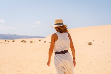 Genç bir turist, Fuerteventura, Kanarya Adaları 'ndaki Corralejo Doğal Parkı sahillerinde kumsalda yürürken şapka takıyor. İspanya
