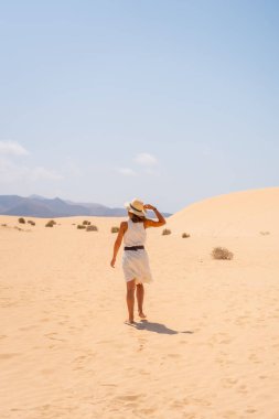 Genç bir turist, Fuerteventura, Kanarya Adaları 'ndaki Corralejo Doğal Parkı sahillerinde kumsalda yürürken şapka takıyor. İspanya