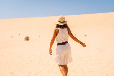 Beyaz elbiseli ve şapkalı genç bir turist Corralejo Doğal Parkı, Fuerteventura, Kanarya Adaları 'nın kumullarında yürüyor. İspanya