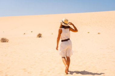 Beyaz elbiseli ve şapkalı genç bir turist Corralejo Doğal Parkı, Fuerteventura, Kanarya Adaları 'nın kumullarında yürüyor. İspanya