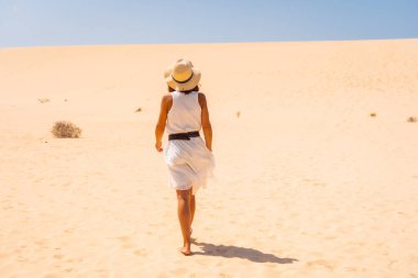 Beyaz elbiseli ve şapkalı turist Corralejo Doğal Parkı, Fuerteventura, Kanarya Adaları 'nın kumullarında yürüyor. İspanya