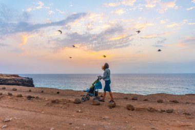Kanarya Adaları, Fuerteventura Adası 'nın kuzeyindeki El Cotillo kasabasında oğluyla birlikte Batı Yakası Fotoğraf Noktasında yürüyen bir anne. İspanya