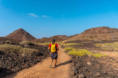 Sarı sırt çantalı genç bir adam kuzeye, Isla de Lobos 'a doğru gidiyor. Fuerteventura adasının kuzey kıyısı boyunca, Kanarya Adaları. İspanya