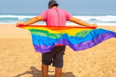 Çölde rüzgarda uçuşan LGBT bayrağıyla tanınmayan bir gay, eşcinselliğin sembolü, gökkuşağı bayrağı