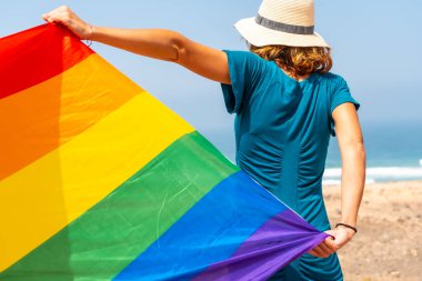 Lgbt sembolü, arkadan tanınmayan yeşil elbiseli, deniz kenarında bayrak sallayan bir lezbiyen.