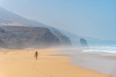 Fuerteventura, Kanarya Adaları 'nın güneyindeki Jandia, Barlovento doğal parkının Coffee plajında tek başına yürüyen şapkalı bir turist kız. İspanya