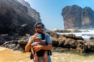 Sırt çantasında bebeğiyle Barlovento, Jandia 'nın doğal parkının Roque del Moro plajında, Fuerteventura, Kanarya Adaları' nın güneyinde genç bir baba. İspanya