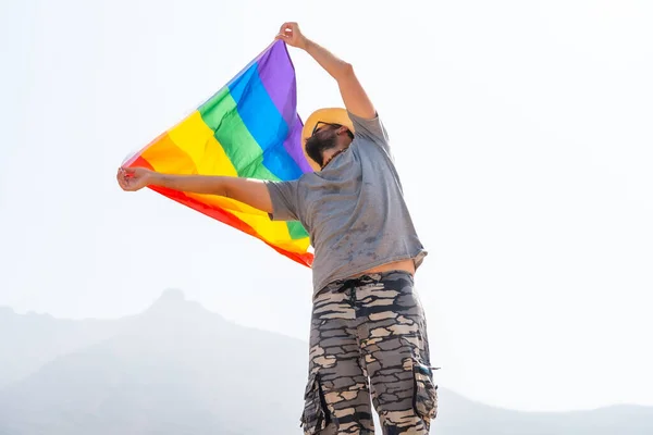 男同性恋 身穿灰色T恤 头戴白色帽子 在乌云密布的天空中挥动Lgbt旗 象征同性恋 — 图库照片