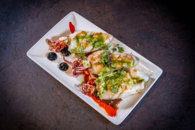 Siyah arka planda, beyaz tabakta soslu kızarmış kalamar.