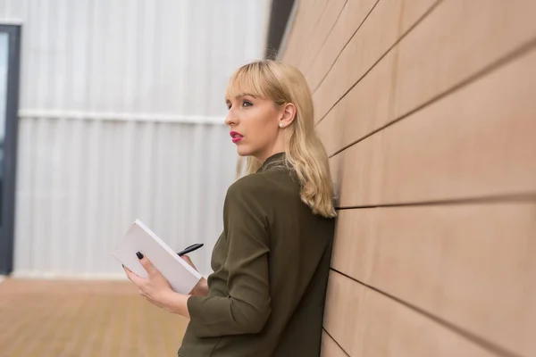 专心致志的商业园企业家女孩指着日记本上的字条 穿着绿色衬衫的年轻金发女郎靠着木墙 — 图库照片