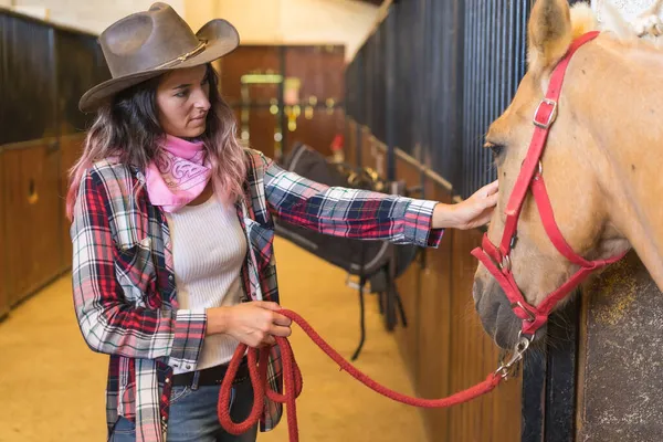 カウガールの女性が馬を安定させ 南ウサの帽子 ピンクのプレイシャツとジーンズを身に着けている — ストック写真