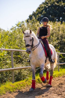 Beyaz bir ata binen, güvenlik şapkalı, siyah atlı, beyaz bir sarışın kız.