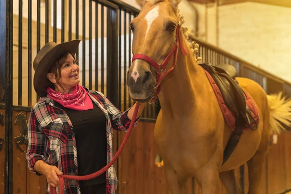 Portrait of an adult woman in the stable of a horse with a brown horse, dressed in South American outfits