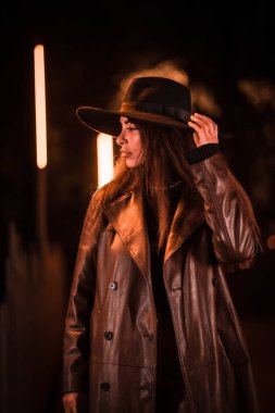 Geceleri parktaki yapay ışığın altında şapka takan bir kız. kış akşamı modası