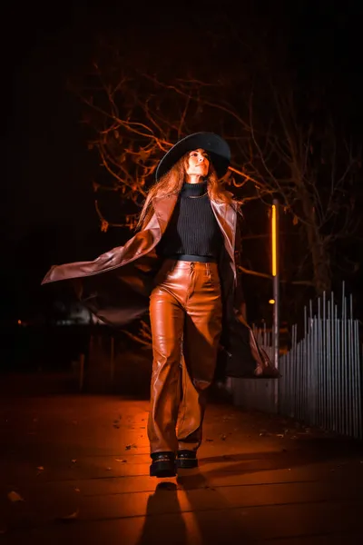 Girl in a hat in a portrait at night in a raincoat on a parcel. Caucasian brunette model looking at camera