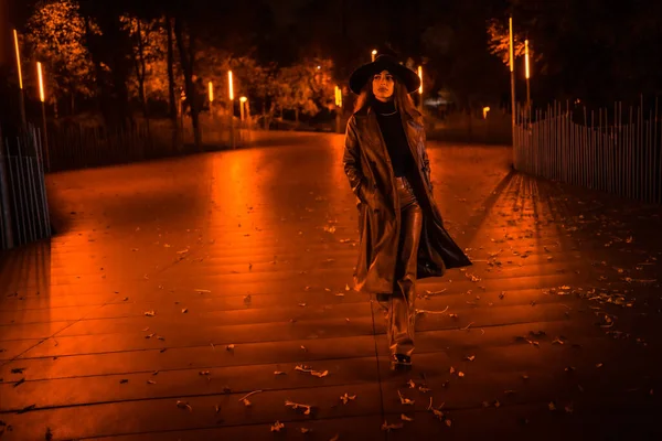 冬天的夜晚 戴着帽子的女孩从容地穿过公园 以时髦的姿态享受夜晚的孤寂 — 图库照片