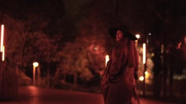 Kafkasyalı esmer kız, gece parkta şapkasıyla yürüyor. Kış akşamı modası