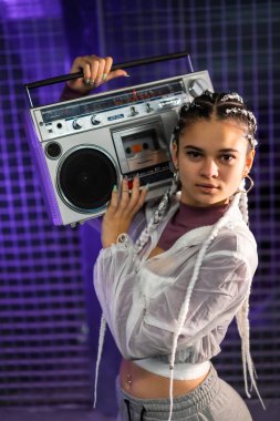Omuzlarında müzik aleti olan beyaz örgülü genç bir kızın portresi, şehir arka planı, mor lekler, 80 'ler tarzı, eski fotoğrafçılık, dikey fotoğraf.