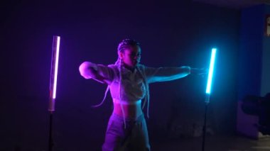 Beyaz örgülü rap dansçısı, neon ışıklarıyla dans ediyor. Video klip kaydediyor. Mavi ve pembe ışıklar, video kameraya bakıyor.
