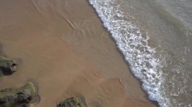 Kayaların yanındaki dalgaların havadan görüntüsü. Dalgalı bir uçakla deniz manzarası, yazın sakin bir denizin dalgaları.