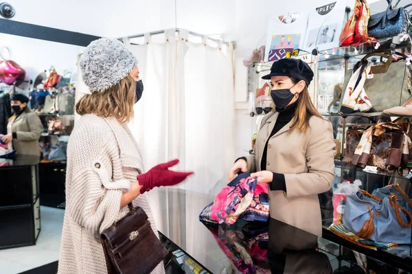 Employee of a clothing store showing clothes to a customer, working with security measures in the coronavirus pandemic. Second hand shop