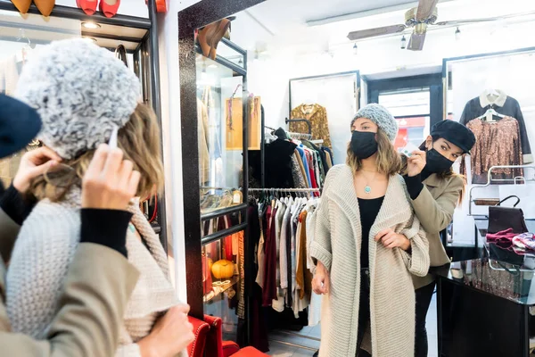 Employee with a mask in a clothing store trying on a jewel to a client, working with security measures in the coronavirus pandemic, covid-19