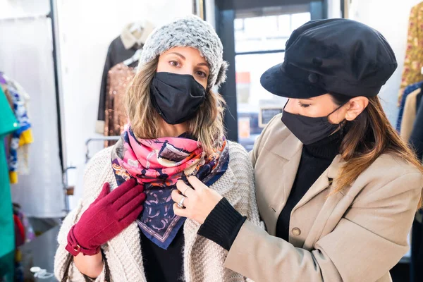 Caucasian employee with a mask from a clothing store testing a customer a pink scarf in a mirror, security measures in the coronavirus pandemic, covid-19