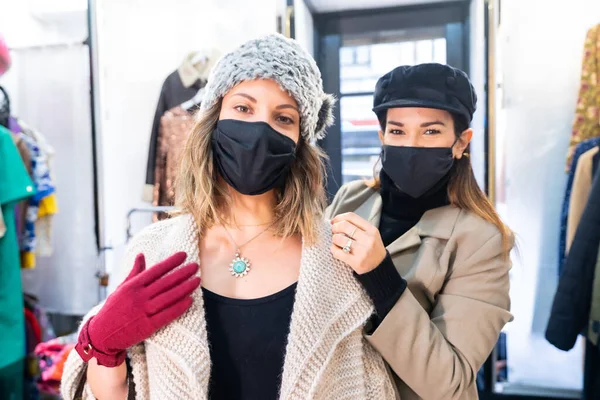 Caucasian employee with a mask from a clothing store trying on a client a jewel in front of a mirror, security measures in the coronavirus pandemic, covid-19