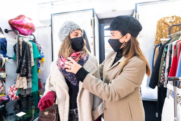 Caucasian employee with a mask from a clothing store testing a customer a pink scarf in a mirror, security measures in the coronavirus pandemic, covid-19