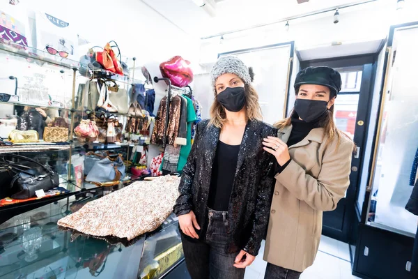 Employee and a client with masks in a luxury clothing store looking at sequin dress, security measures in the coronavirus pandemic, covid-19