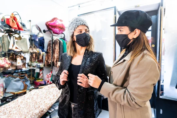 Employee and a client with masks in a luxury clothing store with a sequin dress, security measures in the coronavirus pandemic, covid-19