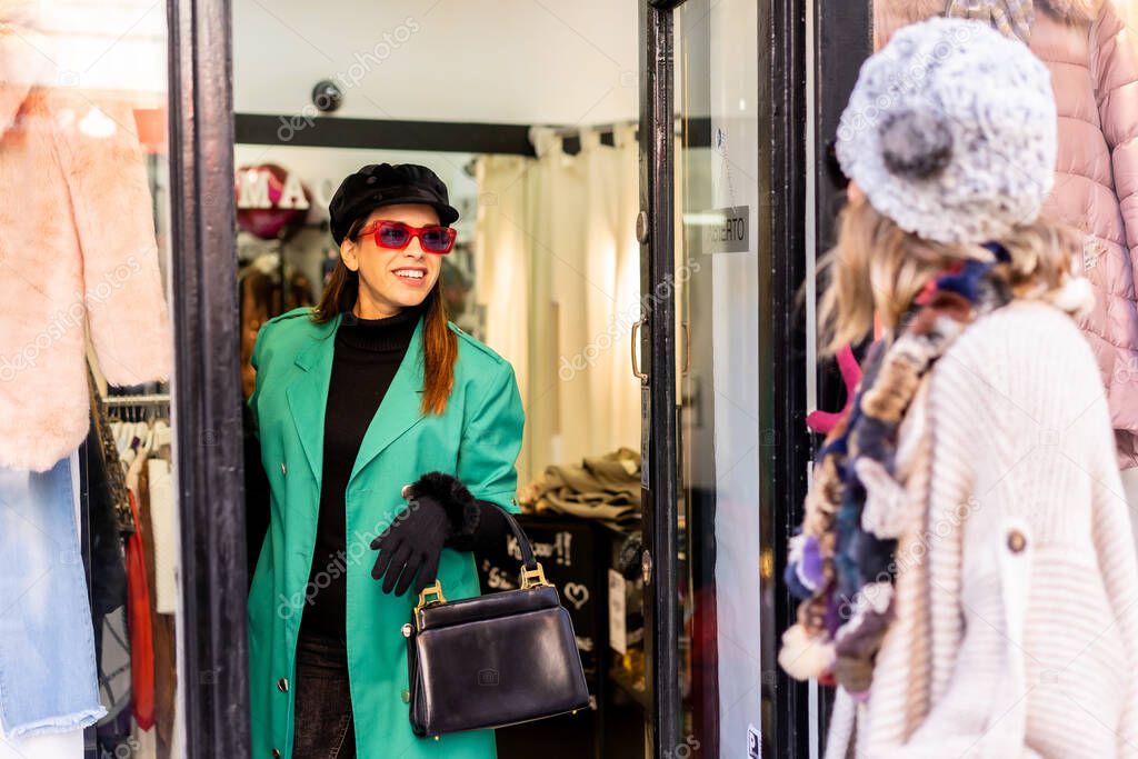 Young Caucasian girl shopping in the city and being attended by a shop assistant, looking at the window of clothing stores. Sunglasses and red gloves